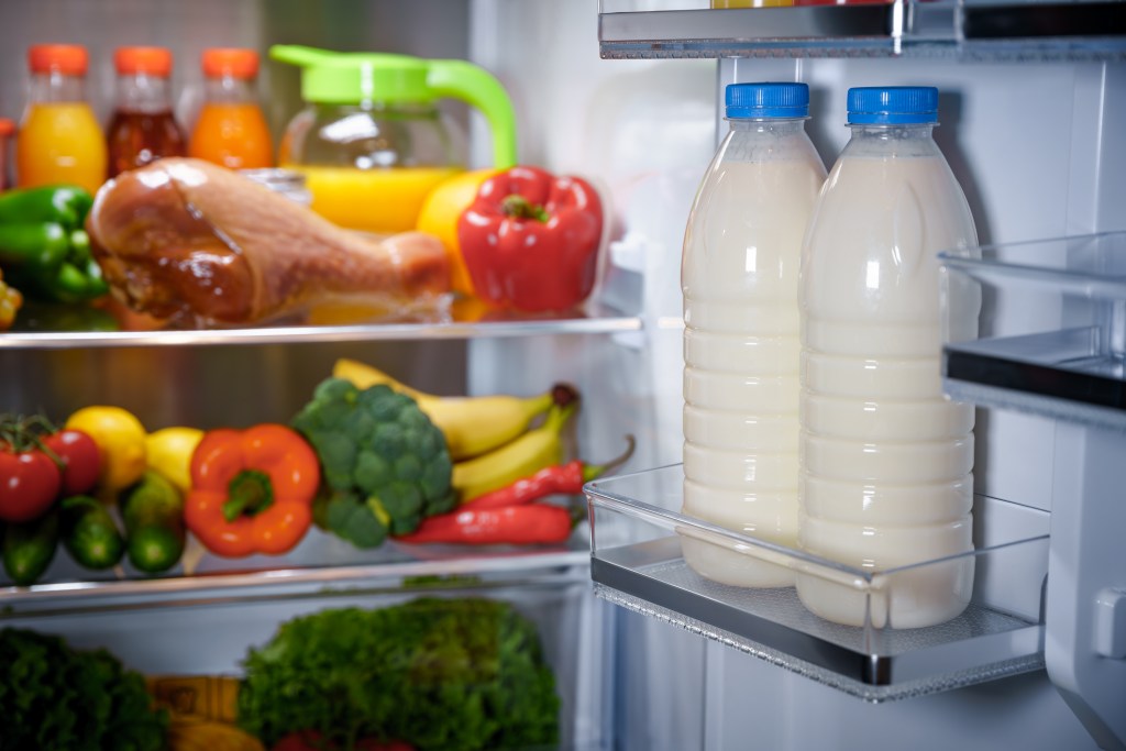 Milk bottles are stored in a full refrigerator, especially placed in the door